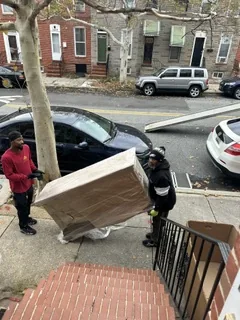 Crew carrying a wrapped sofa down brick rowhouse steps