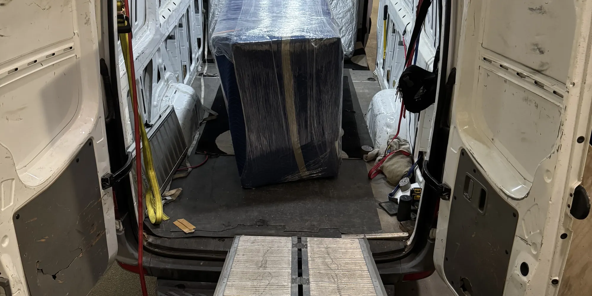 Blanket-wrapped furniture secured in a delivery van at a loading dock